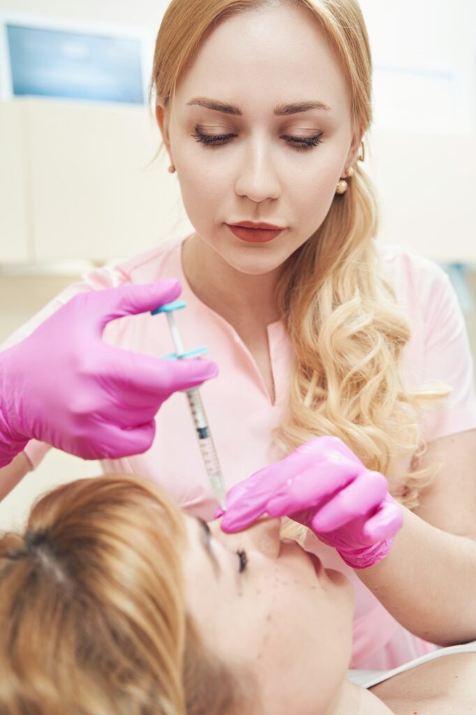 Young beautician with syringe during the procedure of hyaluronic acid in salon